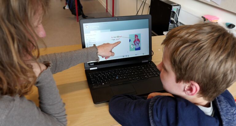 Et barn sidder og læser på en computer med hjælp fra en voksen
